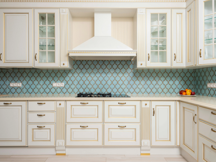 White kitchen cabinets with gold accents and blue patterned tile backsplash