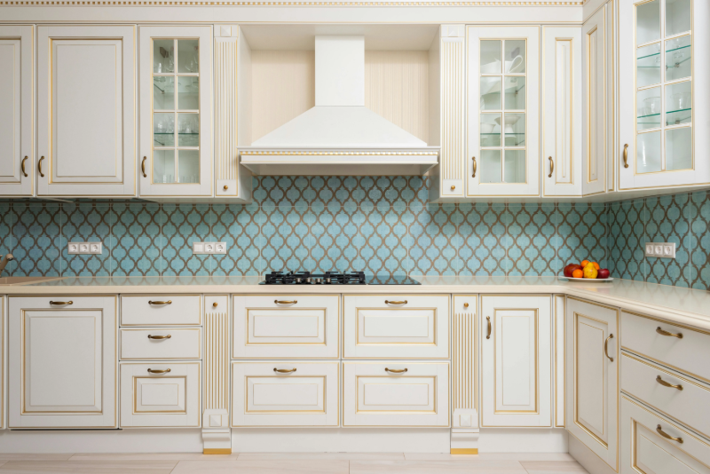 White kitchen cabinets with gold accents and blue patterned tile backsplash